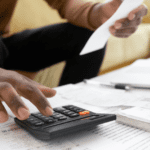 Desk covered in papers and a hand using a calculator